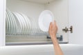 Woman holding clean and white plate near dishware in kitchen cabinet Royalty Free Stock Photo