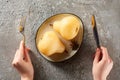 Cropped view of woman holding fork and knife near delicious pear in wine on grey concrete surface