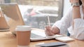 Cropped view of woman holding pen in hand, writing notes in planners, sitting behind wooden table Royalty Free Stock Photo