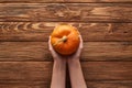 Cropped view of woman holding small ripe pumpkin of wooden surface.