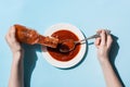 Cropped view of woman holding spoon and pouting delicious tomato sauce in plate on blue background Royalty Free Stock Photo