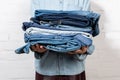 cropped view of woman holding stack of blue denim clothes near white brick wall. Royalty Free Stock Photo