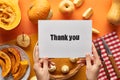 Cropped view of woman holding thank you card near pumpkin pie on orange background. Royalty Free Stock Photo