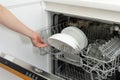 Woman opening modern dishwasher machine with plates and cups, standing on kitchen Royalty Free Stock Photo