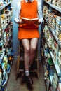 View of woman in orange dress reading book and sitiing on ladder in library