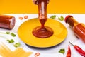 Cropped view of woman pouring ketchup on plate beside spaghetti and chili peppers on white surface isolated on yellow Royalty Free Stock Photo