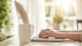 Cropped view of woman sitting at wooden table and working on laptop. A cup of coffee with a potted plant in the