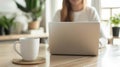 Cropped view of woman sitting at wooden table and working on laptop. A cup of coffee with a potted plant in the