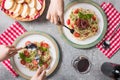 Cropped view of women eating Pappardelle with tomatoes, basil and prosciutto near baguette, red wine on grey surface Royalty Free Stock Photo