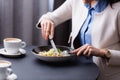 Cropped view of young woman cutting salad near cups of cappuccino on blurred foreground in restaurant.