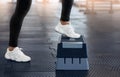 Cropped view of young woman in sports shoes doing exercises with step platform at gym, closeup