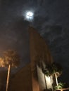 Cross of church appears to light up as full moon shows itself from beyond clouds.