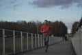 Cross country jogging in countryside. Man in orange sweatshirt running across wooden bridge in national park. Runner Royalty Free Stock Photo