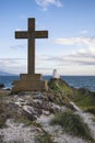 Cross in landscape of Ynys Llanddwyn Island with Twr Mawr lighthouse in background with blue sky