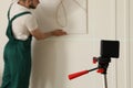 Cross line laser level and handyman hanging picture on white wall