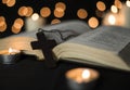 Cross placed on a open bible and candles against bokeh lights background