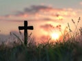 a cross silhouette standing in a field, with the warm glow of a sunset sky Royalty Free Stock Photo