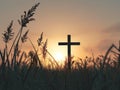 a cross silhouette standing in a field, with the warm glow of a sunset sky Royalty Free Stock Photo