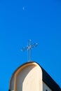 Cross on top of catholic church against deep blue sky and morning crescent