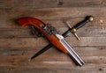 Crossed antique flintlock pistol and large pirate dagger on a rough wooden table