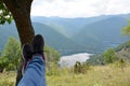 Crossed feet in sport shoes leaning on a tree and a blurred background with mountains and a lake