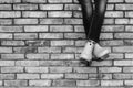 Crossed legs of a young girl in jeans and orange galoshes sitting on a brick wall against a brick wall background