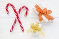 Crossed peppermint candy canes and gift boxes on white wooden background