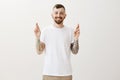 Crossing fingers for luck. Portrait of happy joyful european man with tattoos, wishing or hoping for success of business