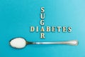 Crossing the words `sugar` and `diabetes`, a spoon with sugar on a blue background, concept.