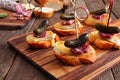 Crostini appetizer skewers with baked brie, sausage and pickles, close up on a serving board against wood Royalty Free Stock Photo