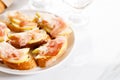 Crostini with cheese, sliced pear and prosciutto on white plate