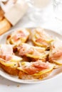 Crostini with cheese, sliced pear and prosciutto on white plate