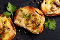 Crostini with melted cheese, mushrooms and fresh parsley on black background