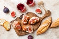 Crostini with prosciutto, cream cheese and figs on wooden board. Appetizers, antipasti snacks and red wine in glasses. Royalty Free Stock Photo