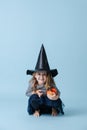 Crouched little girl in witch hat holding small pumpkin, dressed for halloween Royalty Free Stock Photo