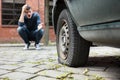 Crouched Man Pointing At Punctured Car Tire Royalty Free Stock Photo