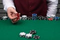 The croupier`s hand is holding red dice over the green cloth of the poker table