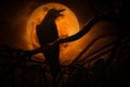 Crow sit on dead tree trunk and croak over fence, old grunge castle, moon and cloudy sky, Mysterious background, Halloween concept