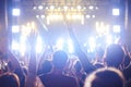 Crowd of audience with hands raised at a music festival. Lights streaming down from above the stage Royalty Free Stock Photo