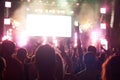 Crowd of audience with hands raised at a music festival. Lights streaming down from above the stage Royalty Free Stock Photo