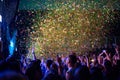 Crowd of audience with hands raised at a music festival. Lights streaming down from above the stage