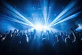 crowd at concert with raised hands in front of bright stage lights, night club under blue rays beam and young people holding light Royalty Free Stock Photo