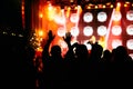 Crowd at a music concert, audience raising hands up in front of bright stage lights.