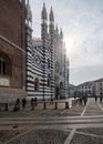 Crowd of people ambling past the towering Monza Cathedral on a sunny day. Italy.