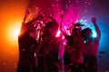 A crowd of people in silhouette raises their hands on dancefloor on neon light background