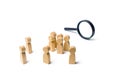 A crowd of wooden human figure stands near a magnifying glass on a white background. The concept of the search for people and Royalty Free Stock Photo