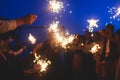 A crowd of young happy people with bengal fire sparklers in their hands during birthday celebration