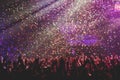 A crowded concert hall with scene stage lights, rock show performance, with people silhouette, colourful confetti explosion fired