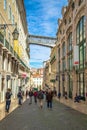 A crowded street and covered gallery of Santa Justa tower over buildings in Lisbon.