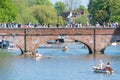 Crowds of people walkingt across arched bridge with multiple small boats passing underneath